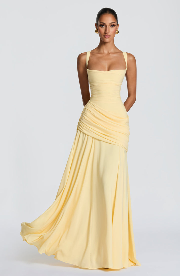 Pale yellow chiffon maxi dress worn by a model, front view with a flowing skirt, draped hip and square neckline.