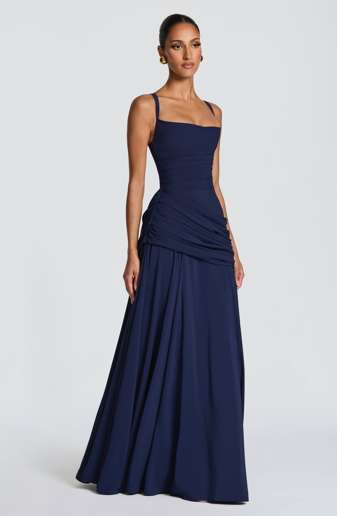 Navy blue maxi dress in a side view with thin straps, ruched waist, draped hip and wide flowing skirt.