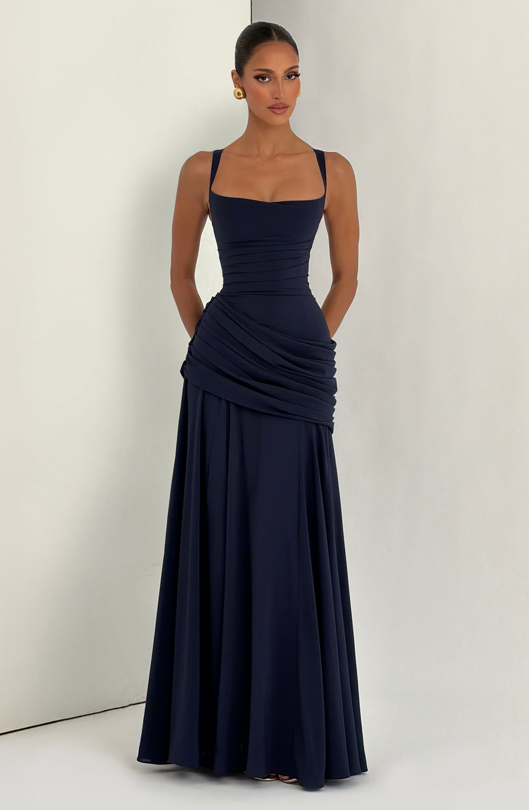 Navy dress full length, model standing against a plain wall with hands tucked into the pockets 11