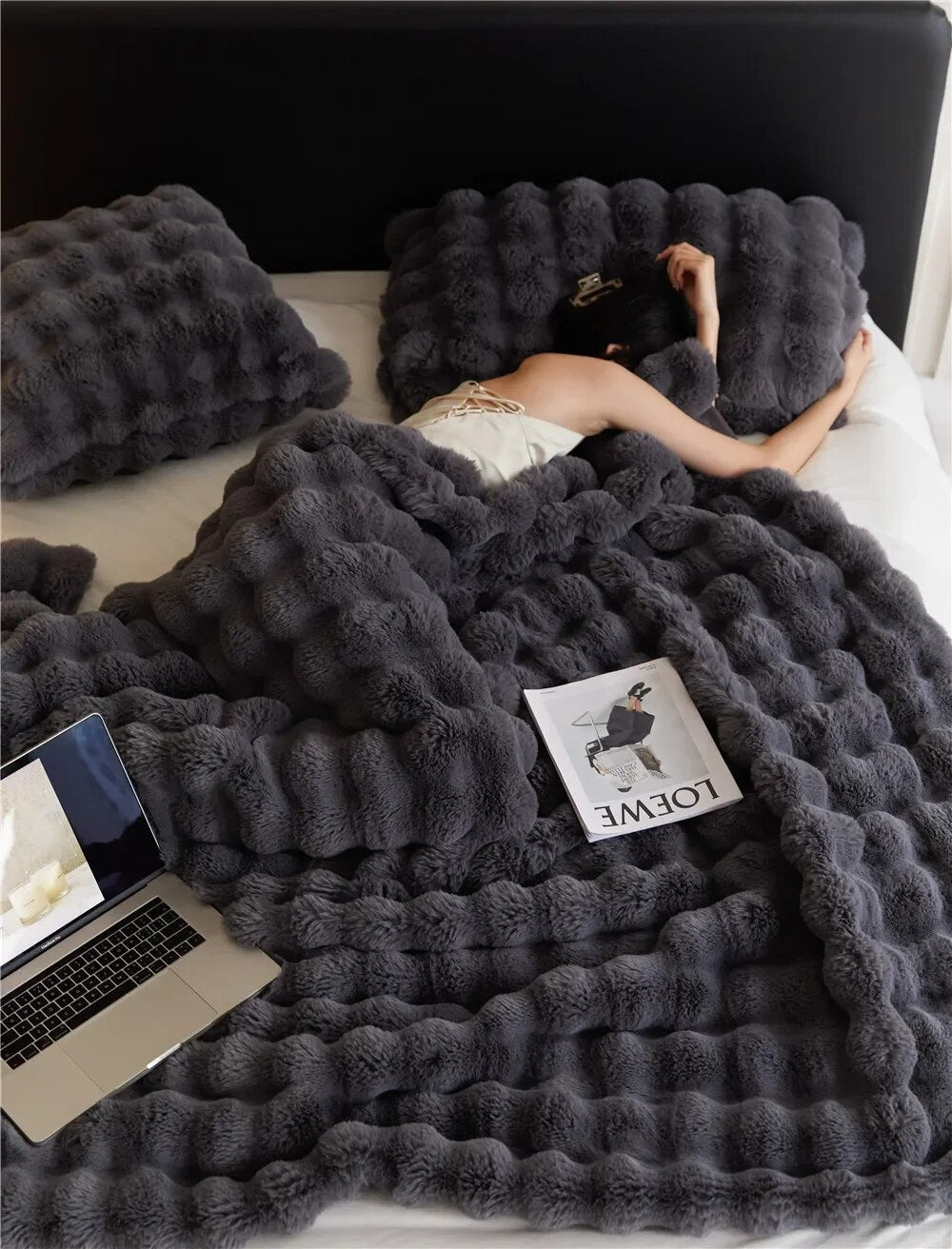 Dark gray bubble-textured blanket covers a bed, with a laptop and a magazine resting on top 3
