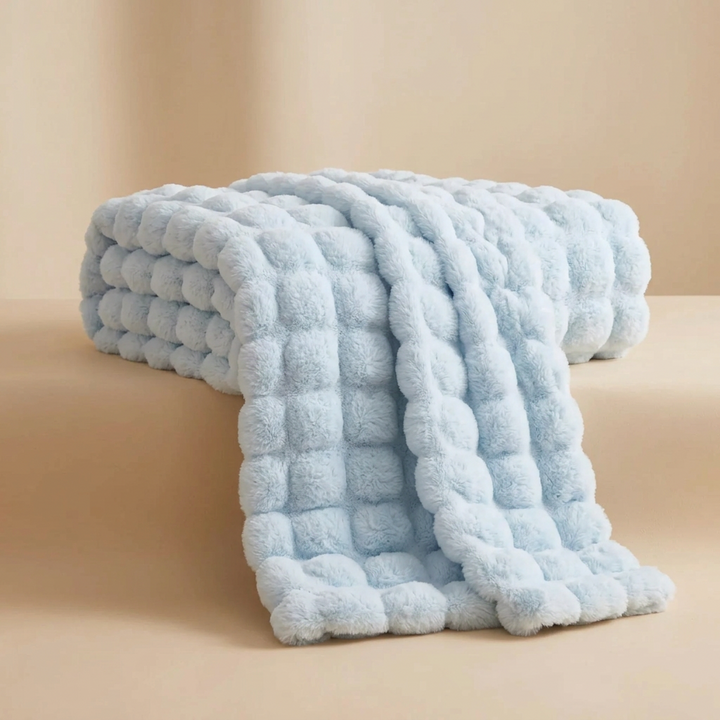 Light blue bubble-textured plush blanket folded and draped off the edge of a beige ledge 17