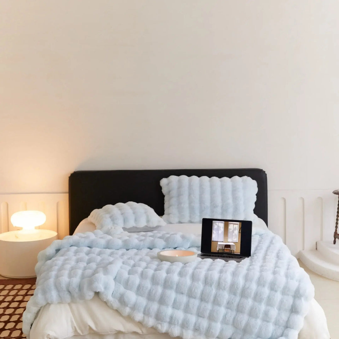Bed with a light blue plush bubble-textured throw and matching pillows, a laptop and candle bowl on top 6