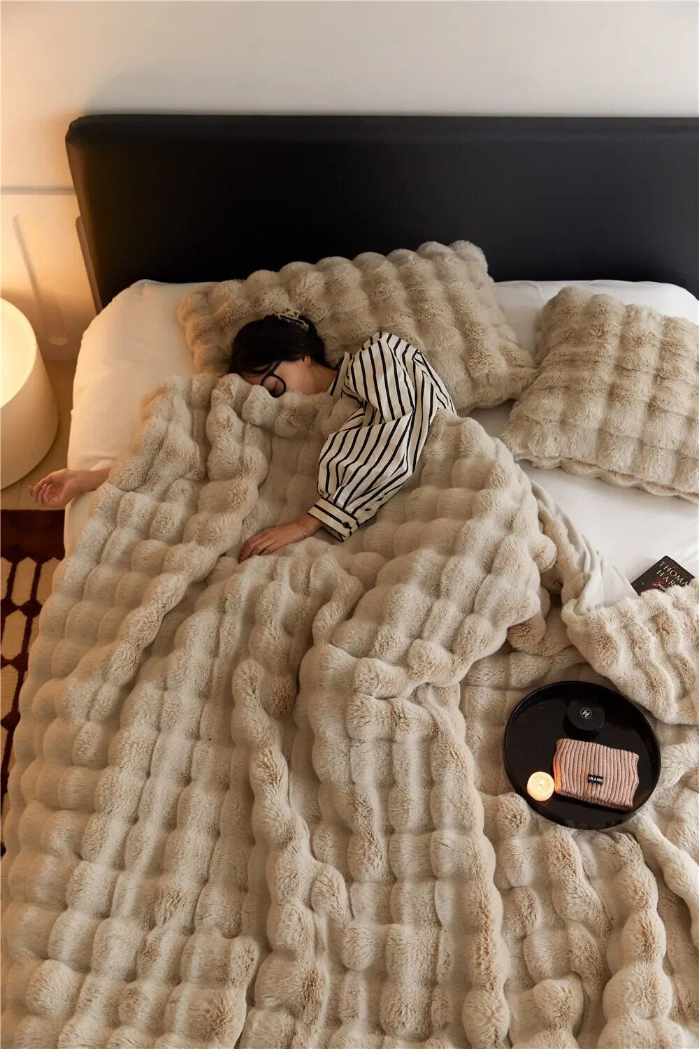 Woman in striped pajamas sleeping on a bed under a tan bubble-textured plush throw with matching pillows 2
