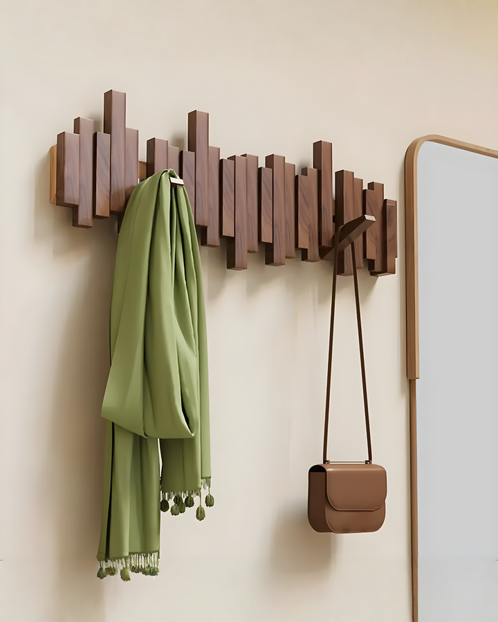 Dark wooden staggered-bar rack beside a mirror, with a green tasseled scarf on one hook and a small brown crossbody bag on another.