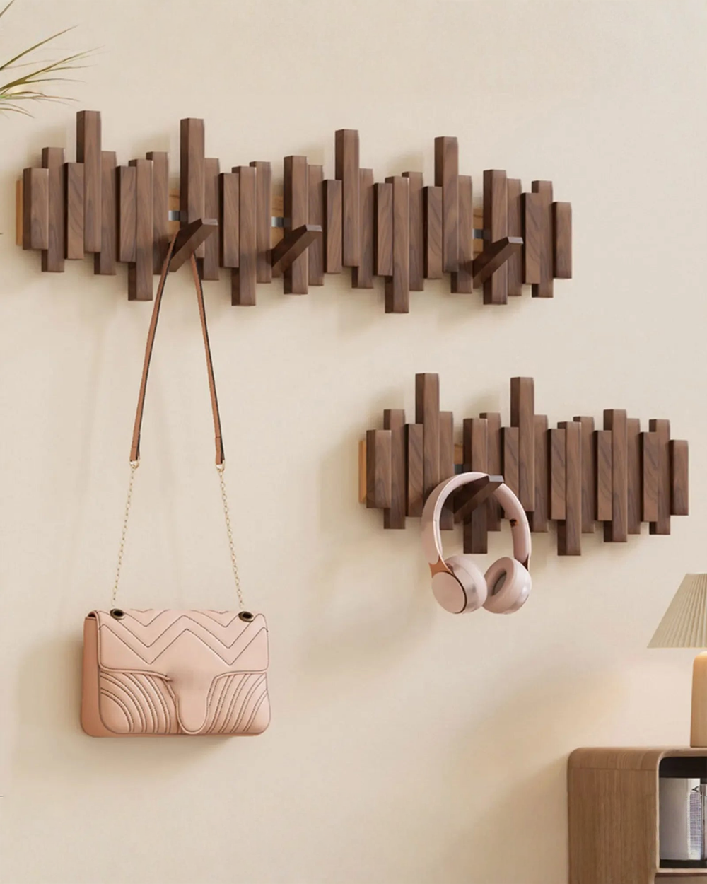 Two dark wooden wall racks of different lengths side by side, one holding a pink quilted shoulder bag, the other holding pink headphones.