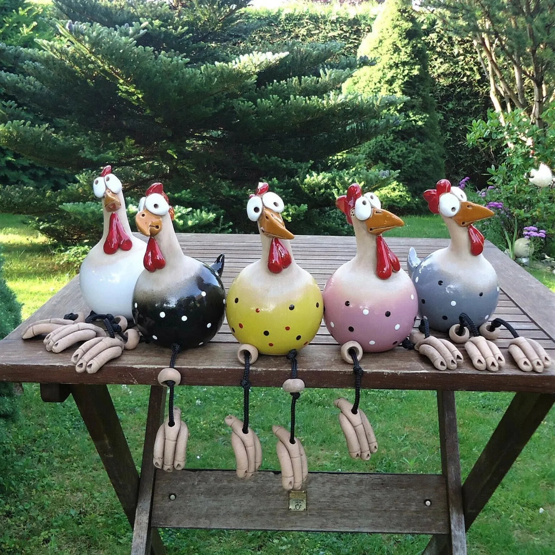 Five glazed ceramic chicken figurines in white, black, yellow, pink and gray with polka dots sit in a row on a wooden garden table. 1