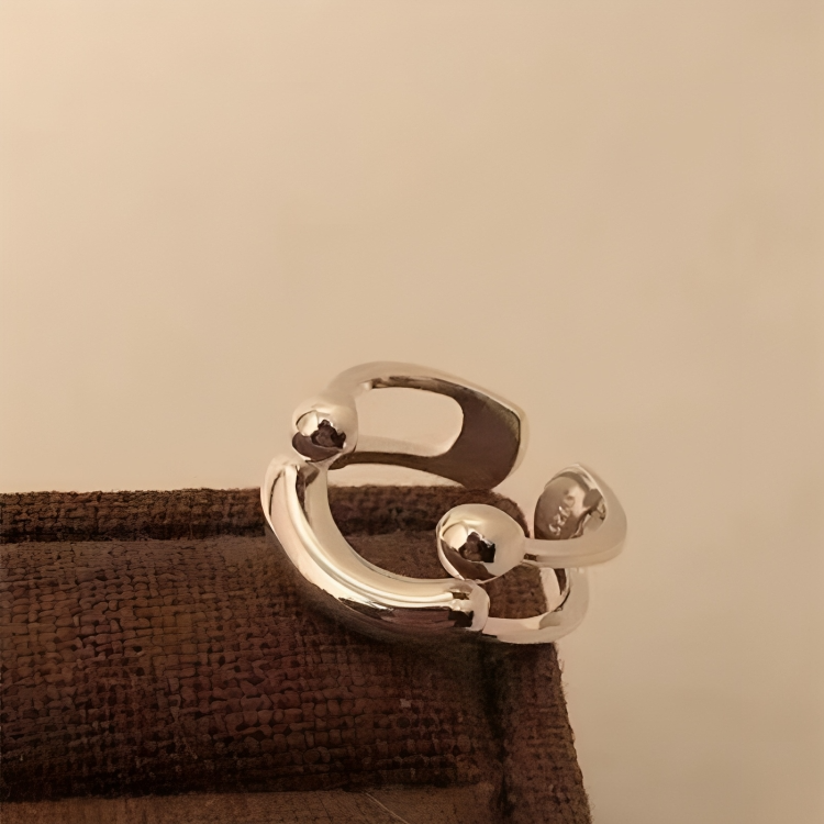 Angled close-up of the polished silver ring resting on a brown woven surface, showing the ball ends and open back. 5