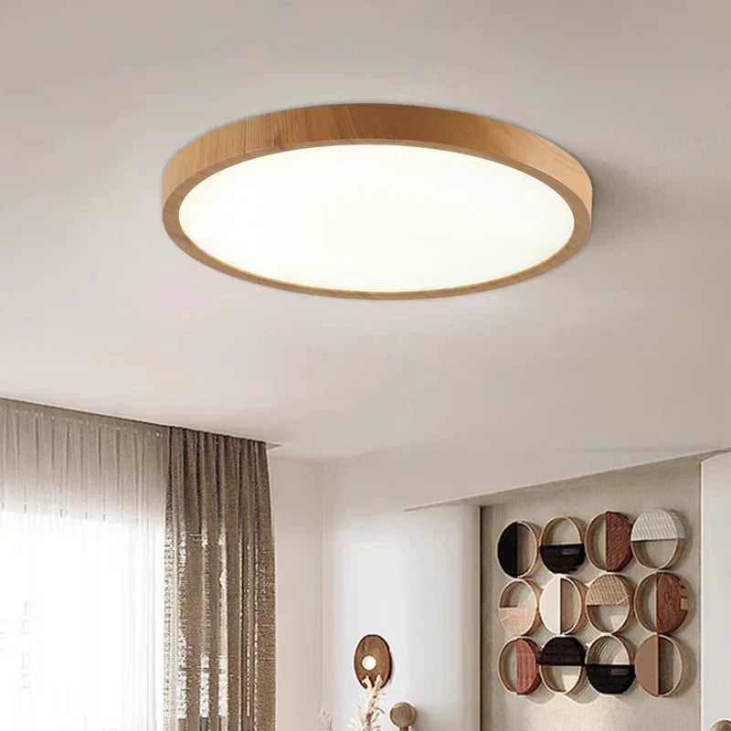 Light-wood round flush ceiling lamp lit above a bright room, with curtains at left and circular wall art at right. 2