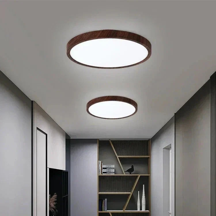 Two dark wood-framed round ceiling lights in different sizes lighting a gray hallway with a bookshelf at the end. 5