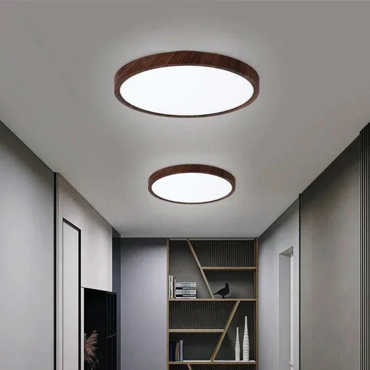 Two dark wood-framed round ceiling lights in different sizes lighting a gray hallway with a bookshelf at the end. 5
