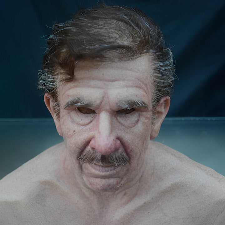 Middle-aged to elderly man mask with swept brown-gray hair, gray mustache and drooping eyelids on a dark teal background