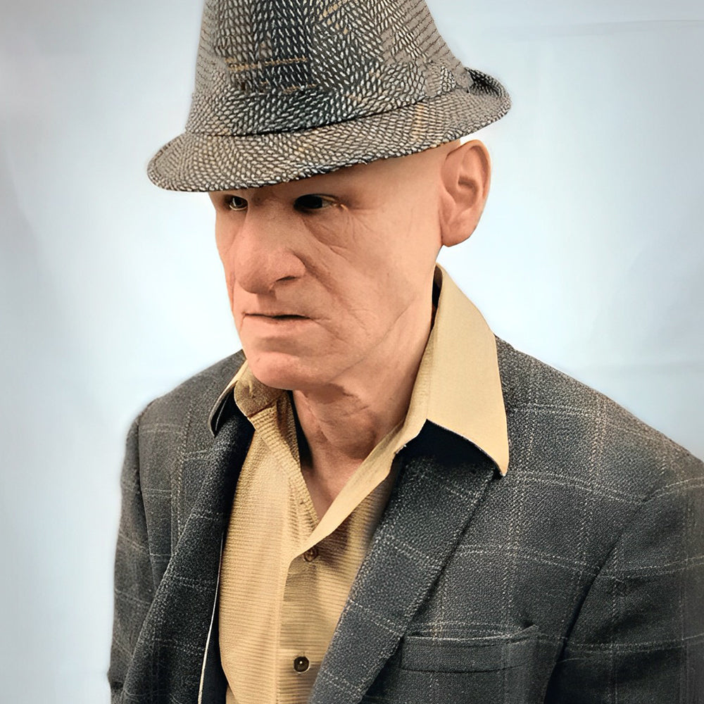 Elderly man mask worn by a model in a patterned fedora, plaid blazer and tan shirt another view