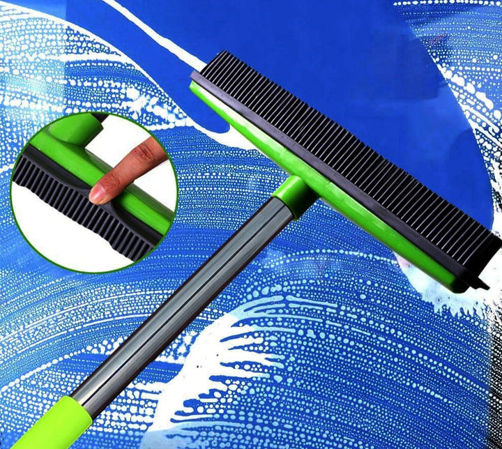 Green and black broom head pressed against a soapy blue window with an inset circle showing the rubber squeegee edge.