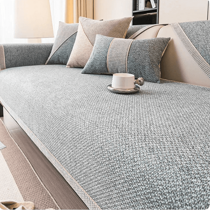 Gray woven couch cover with a braided trim edge on a sofa, with matching throw pillows and a white cup on a tray. 1