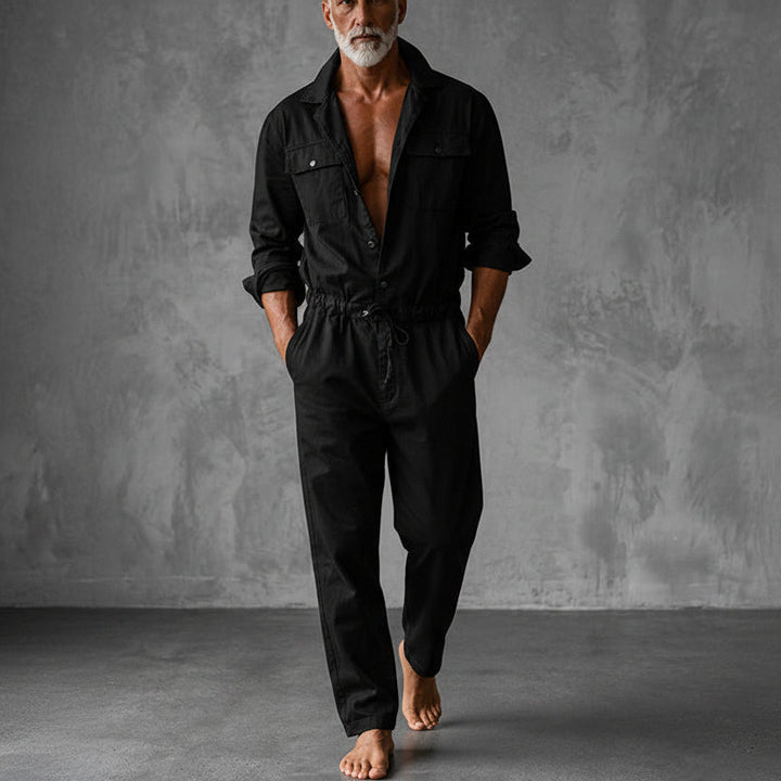 Barefoot man in a black version of the jumpsuit with chest pockets, walking in a studio 3