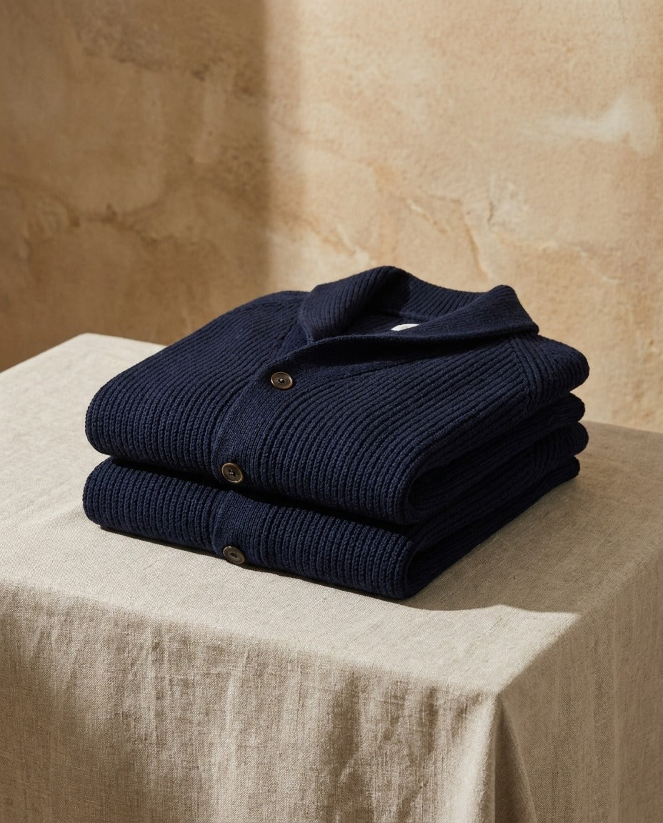 Two folded navy cardigans stacked on a linen-covered table in front of a textured sand-colored wall 10