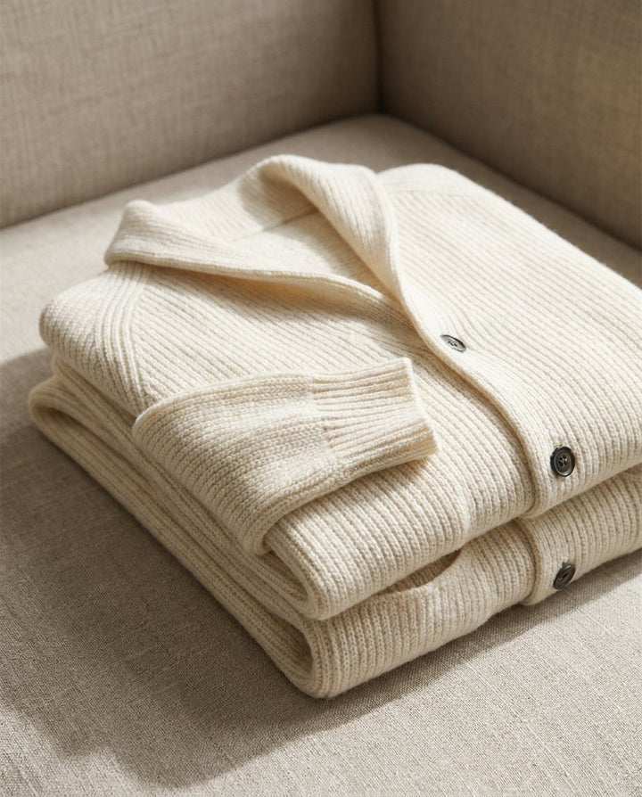 Two folded cream cardigans stacked on a beige sofa, showing the thick rib knit, collar and dark buttons 8