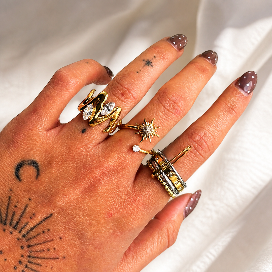 Another view of the wavy gold ring worn on the hand with two clear stones on the index finger.