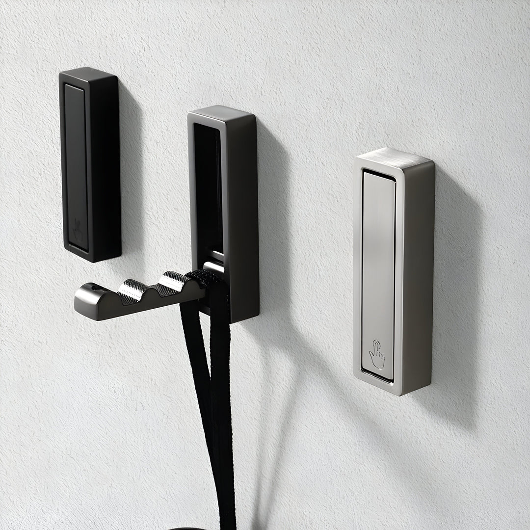 Three square-edged Hidden Wall Hooks on a textured gray wall in black, dark gray and silver, the middle one folded out holding a black strap.