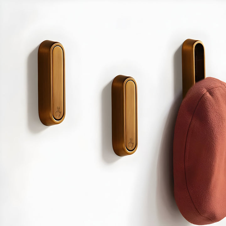 Three bronze rounded Hidden Wall Hooks on a white wall, the one on the right open with a rust-red cap hanging from it.