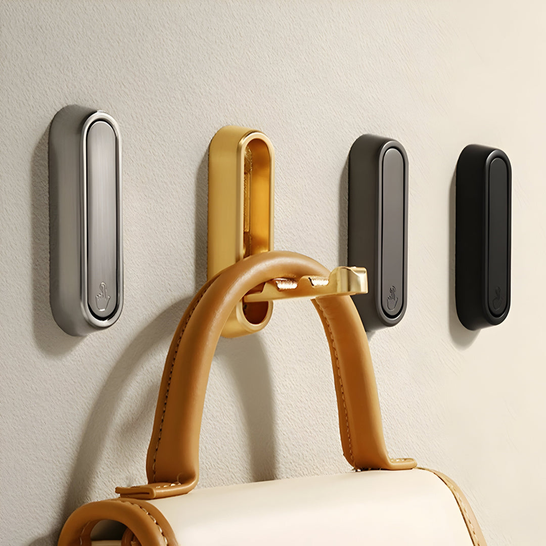 Four rounded Hidden Wall Hooks in silver, gold, dark gray and black on a textured wall, the gold one holding a tan leather handbag.