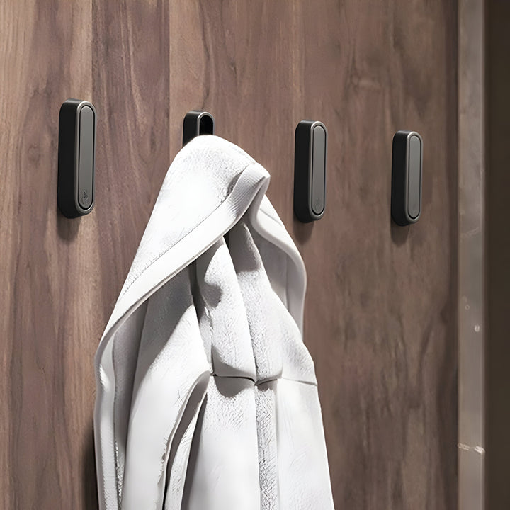 Four rounded Hidden Wall Hooks in black and gray on a wood-paneled wall, one open with a white towel hanging from it.