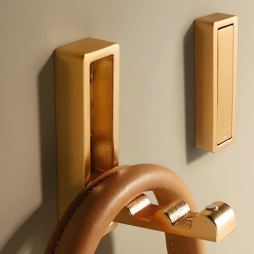 Hidden Wall Hooks in gold stainless steel mounted on a beige wall, one folded out holding a tan leather bag handle.