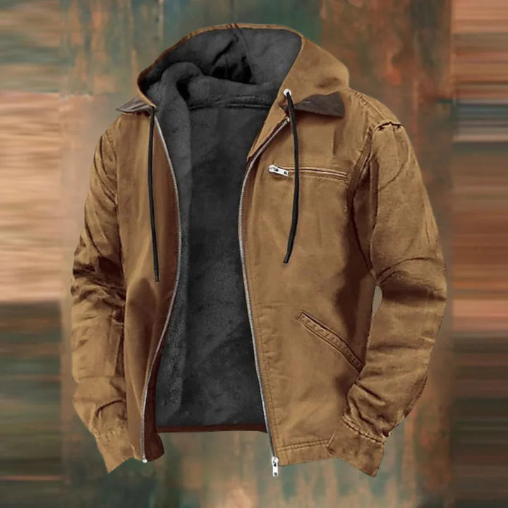 Unzipped tan-brown hooded jacket with drawcords, zippered chest pocket, slanted hand pocket and dark fleece lining, shown against a blurred wood-toned backdrop. 1