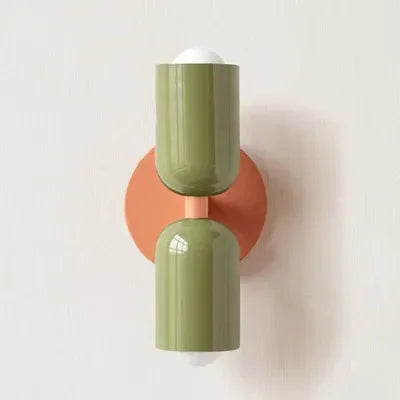 Wall lamp with olive green shades on a round coral-orange backplate, one shade pointing up and one down, mounted on a white wall. 21