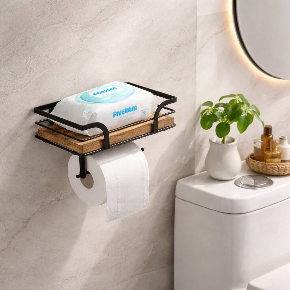 Toilet paper holder detail beside a toilet tank, with wet wipes on the wooden shelf above the paper roll.