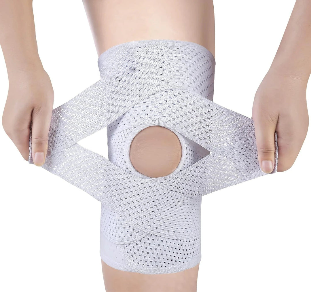 Both hands pulling apart the crossed straps of a light gray perforated knee wrap, showing the open kneecap hole on a white background. 10