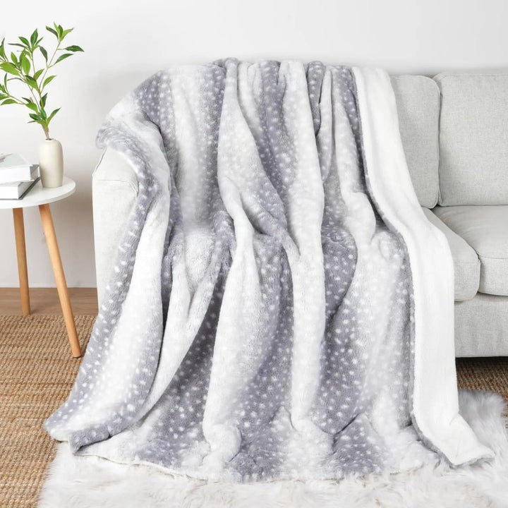 Gray and white version of the spotted throw draped over a light sofa, with the white sherpa side visible.