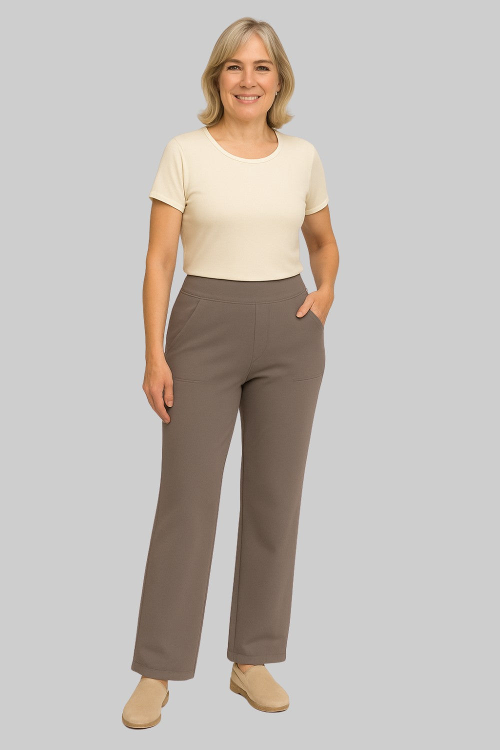 Women's taupe-brown straight-leg pants, cream short-sleeve top and beige slip-on shoes, one hand in pocket, full-length front view.