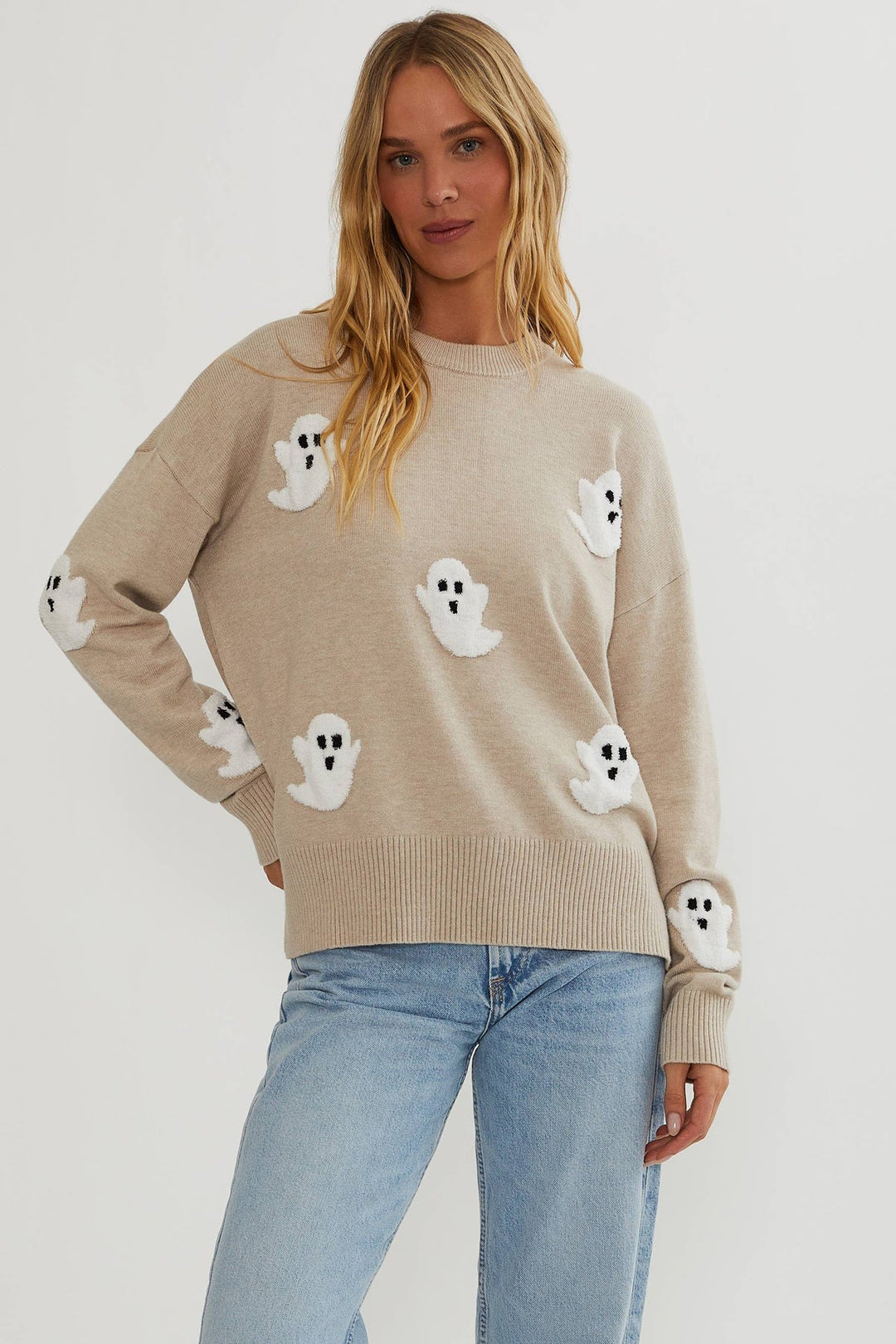 Woman in a beige knit pullover with fuzzy white ghost appliques, styled with light-wash jeans, front view 1