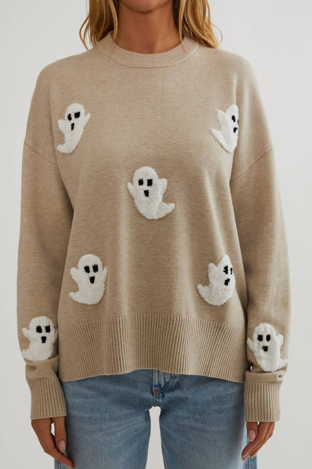 Close front view of the oatmeal knit sweater showing textured white ghost appliques and ribbed hem and cuffs 2