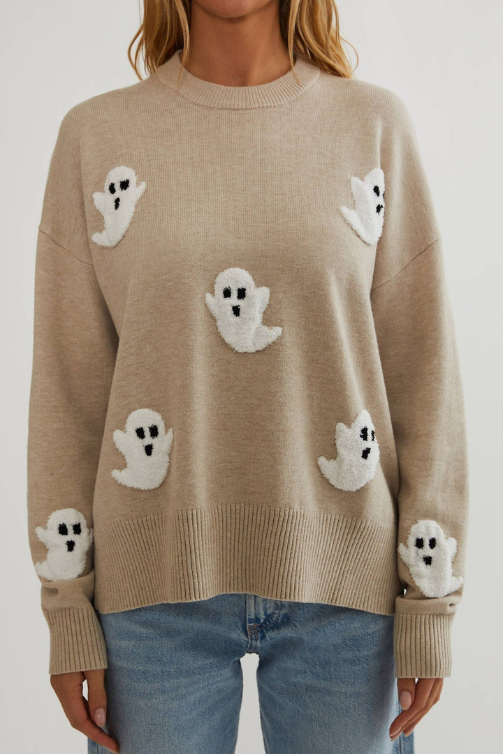 Close front view of the oatmeal knit sweater showing textured white ghost appliques and ribbed hem and cuffs 2