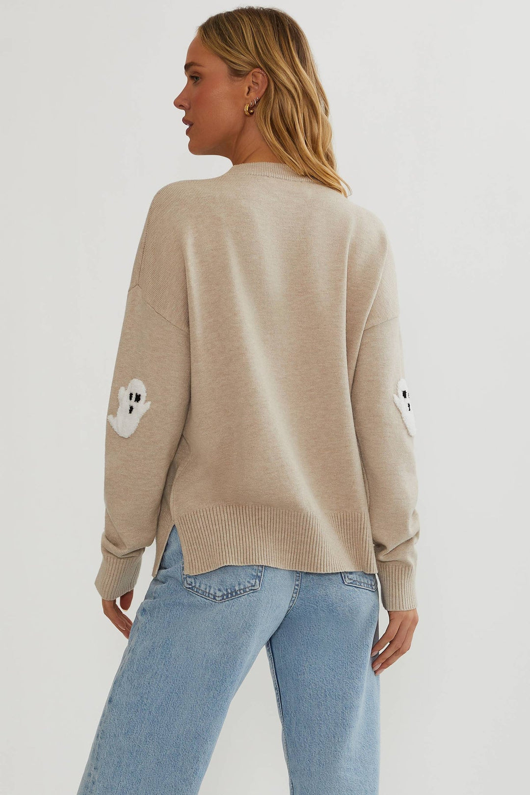 Back view of the beige sweater on a model, showing ghost appliques on the elbows and side slits 5
