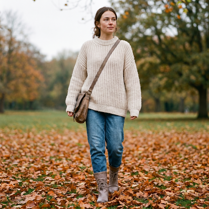 Gray lace-up boots with jeans, cream knit sweater and crossbody bag in a park.