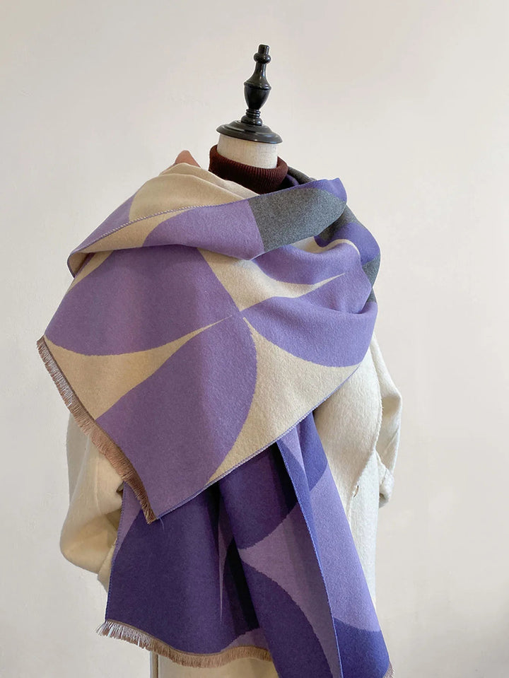Purple, cream and gray geometric scarf draped over the shoulders of a mannequin in a cream coat, fringed ends visible. 1