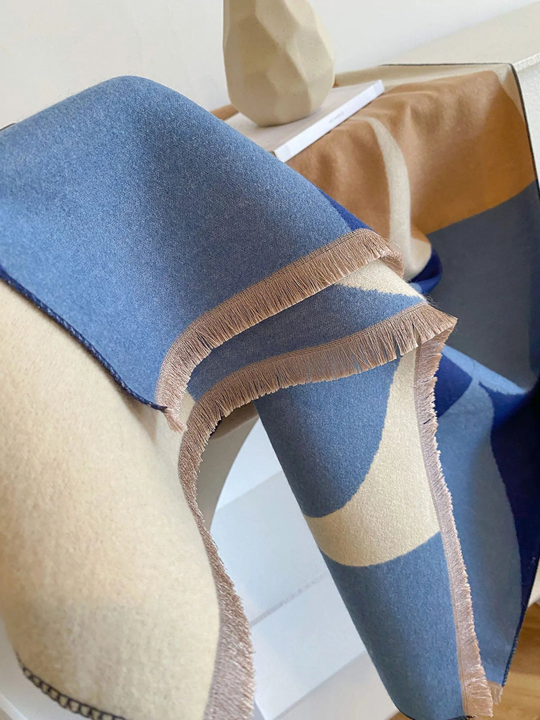 Close-up of the blue, cream and camel scarf's tan fringe and soft surface, draped over a mannequin shoulder. 12