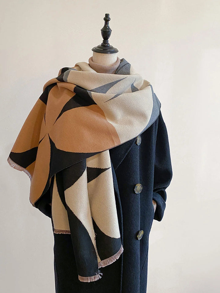 Camel, black, cream and gray geometric scarf wrapped around a mannequin wearing a long black button-up coat. 2