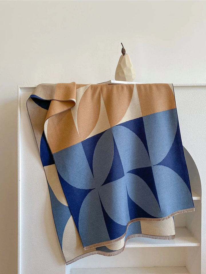 Blue and camel scarf with a bold geometric pattern draped over a white shelf next to a small pear sculpture. 7