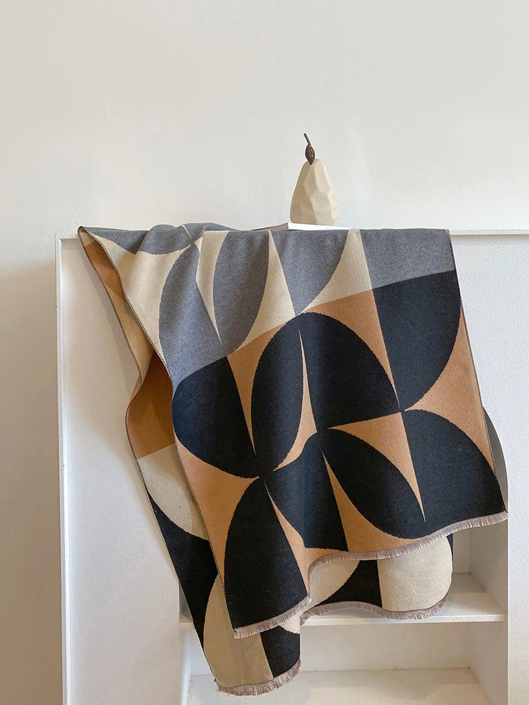 Black, camel, gray and cream geometric scarf hanging over a white shelf with a pear ornament on top. 8