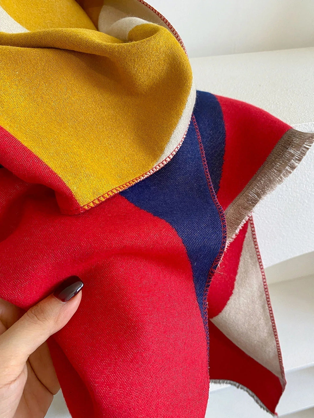 Close-up of the red, navy and mustard scarf fabric held by a hand, showing the contrast stitching along the edges. 9