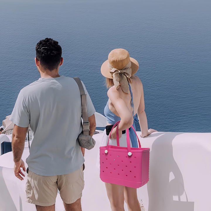 Hot pink perforated tote carried by a woman beside a man overlooking the sea.