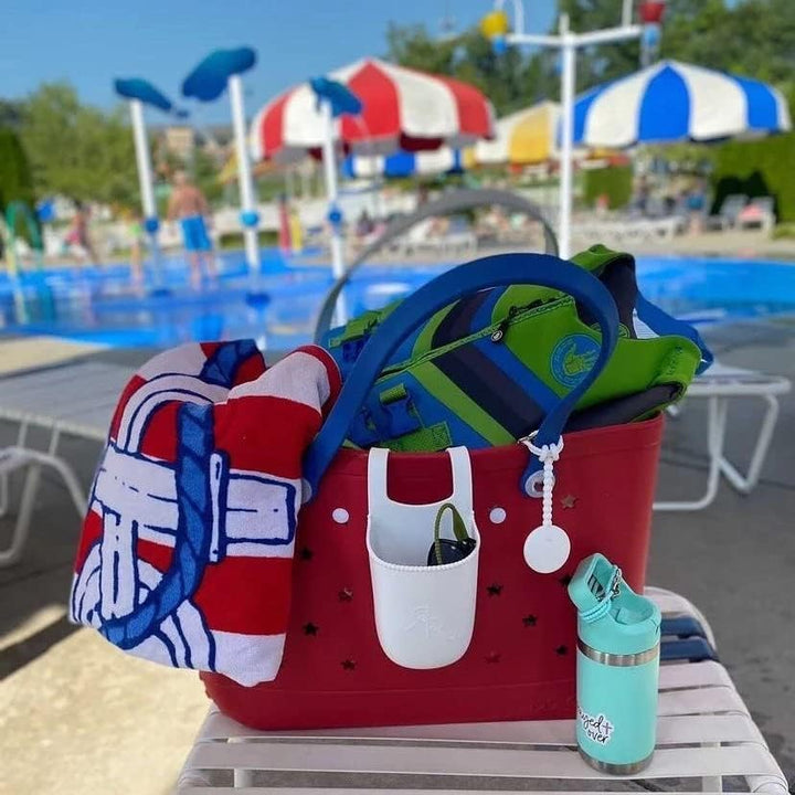 Red tote at a pool packed with a striped towel and a life vest, with a white pocket and a teal bottle. 24