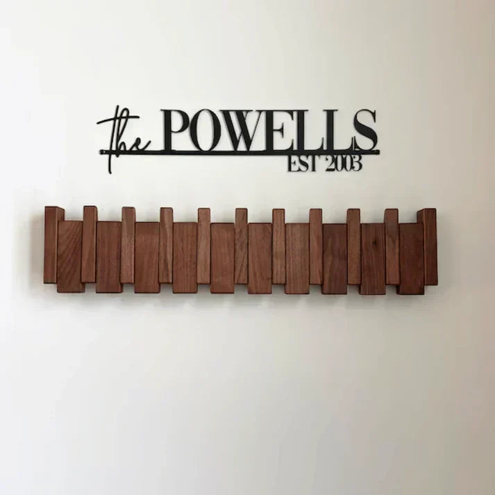 Dark wood rack with all hooks folded flat, mounted on a wall beneath a black metal family name sign 6