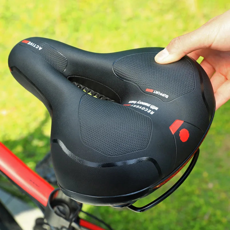 Hand holding the black saddle with red details, showing the textured grip panels and center cutout.