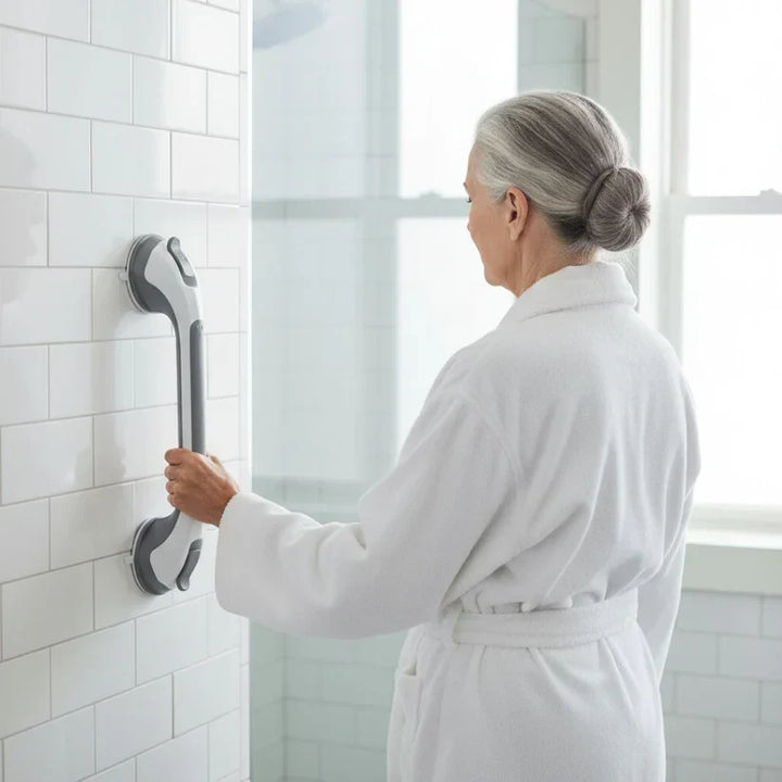 Older woman in a white robe holds the grab bar mounted vertically on a tiled shower wall.