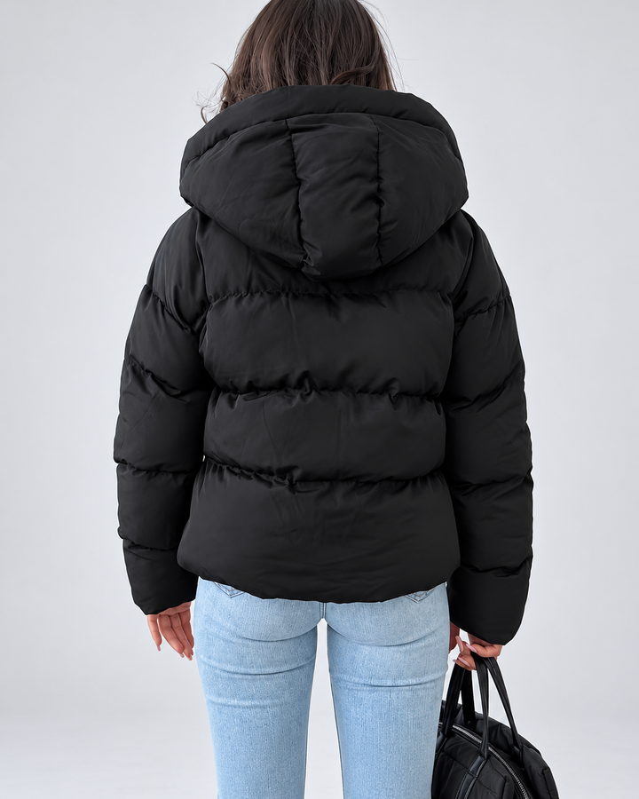 Back view of the black puffer jacket on a model, showing the padded hood and horizontal quilted channels.